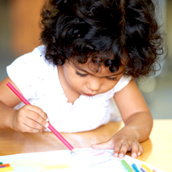 little girl writing on paper with colored pencil