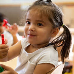 niña sosteniendo crayones y sonriendo