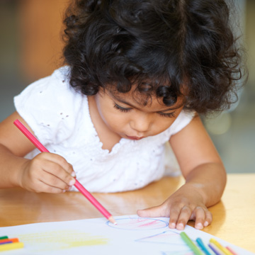 niña pequeña escribiendo en un papel con un lápiz de color